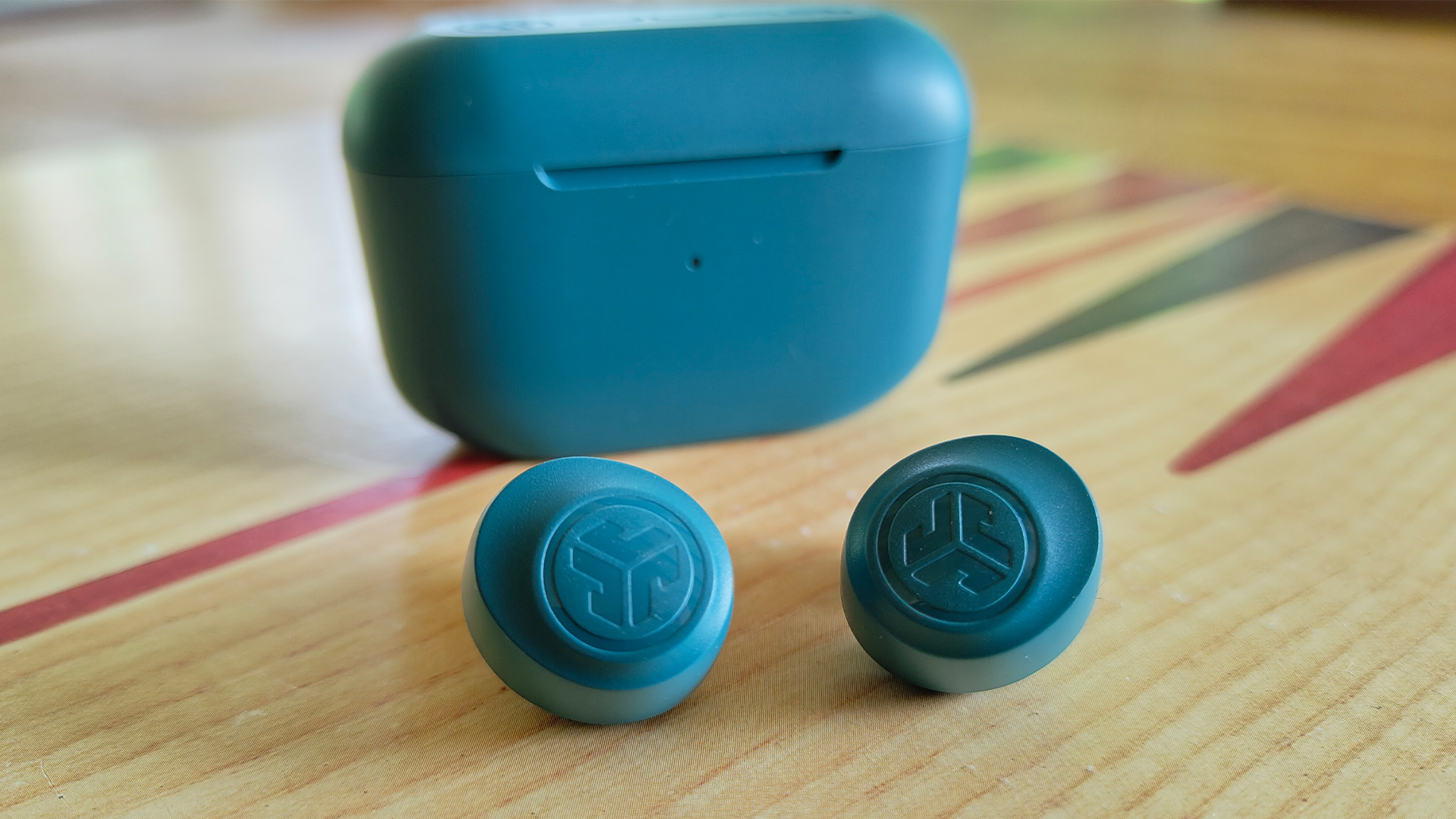 JLab Go Pop+ in-ear headphones in front of charging case on wooden surface