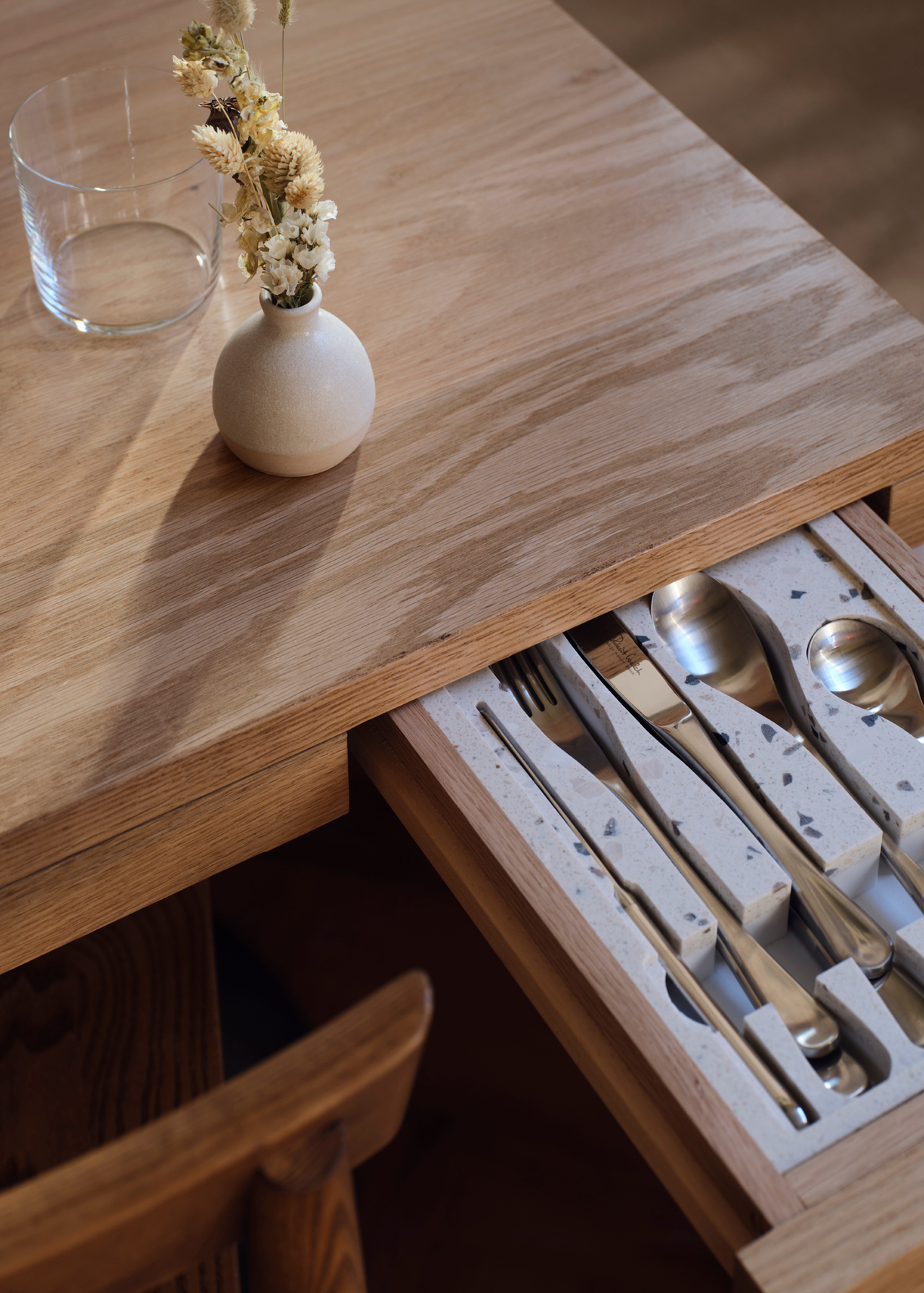 A close-up of a wood dining table with a storage drawer featuring a cutlery insert