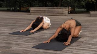 Two women on yoga mats leaning forward into child's pose