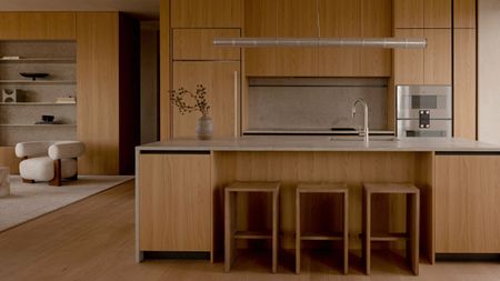 modern timber kitchen with stone countertop and backsplash, three timber bar stools, integrated appliances, a vase with branches on the counter, and chrome tap