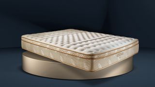 The Saatva Classic Mattress photographed on a round gold plinth and placed on a moody dark blue to black background