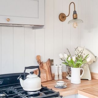 country kitchen ideas, country kitchen with white tongue and groove on walls, classic range, enamel kettle, brass wall light, enamel jug with flowers, wood worktop