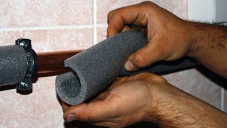 Man covering metal pipe with foam insulation sleeve