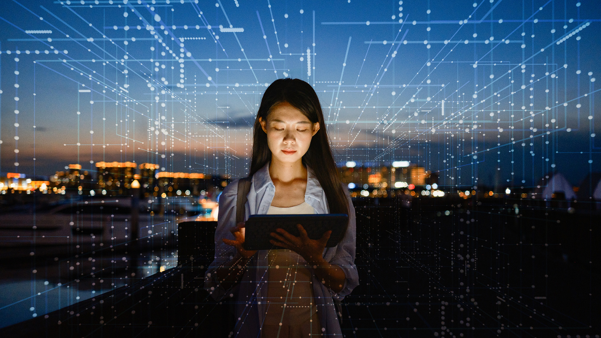 A photo of a woman in cybersecurity holding a tablet, surrounded by a dark cityscape lit with holographic data points.
