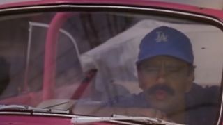 Cheech Marin in a car, wearing a Dodgers hat