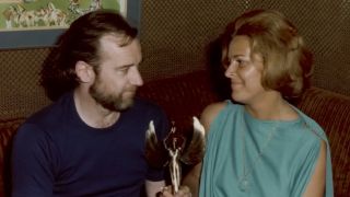 Archival footage of George Carlin and his wife, sitting, holding an award he won for performing. Footage from HBO's documentary George Carlin's American Dream.