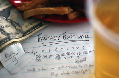Group of fantasy football draft elements which includes draft paper, pick, money, food and beer.