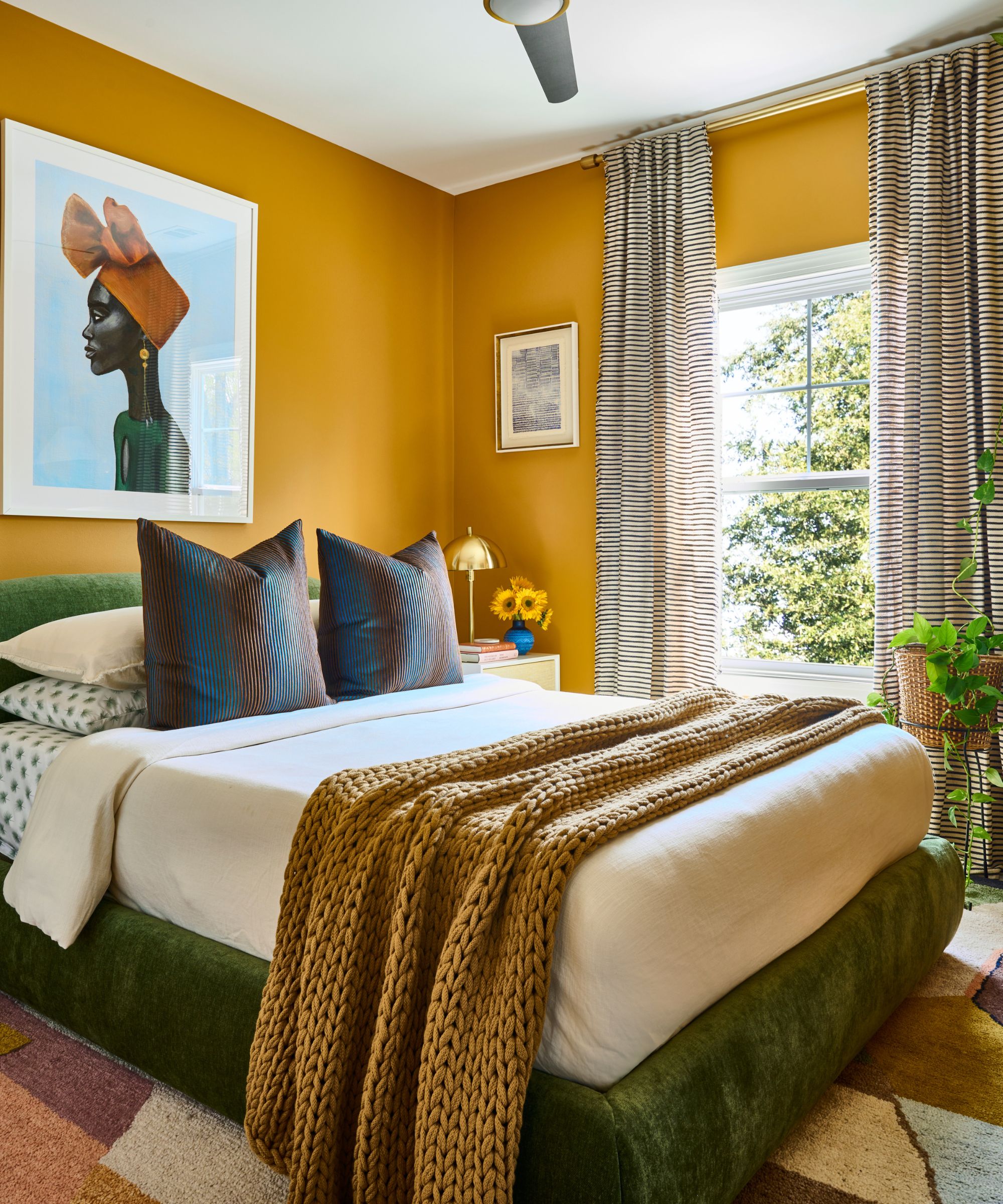 A guest bedroom with yellow walls, a velvet green bed, and patterned accessories