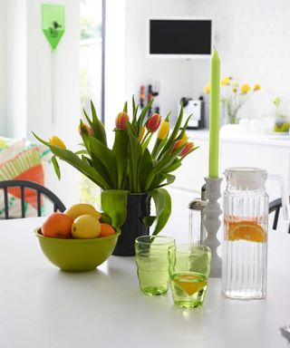 Tulip flowers in a vase alongside orange and lemon citrus fruit in bowl on white kitchen surface