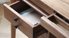 an open desk drawer on a wood desk with black handles