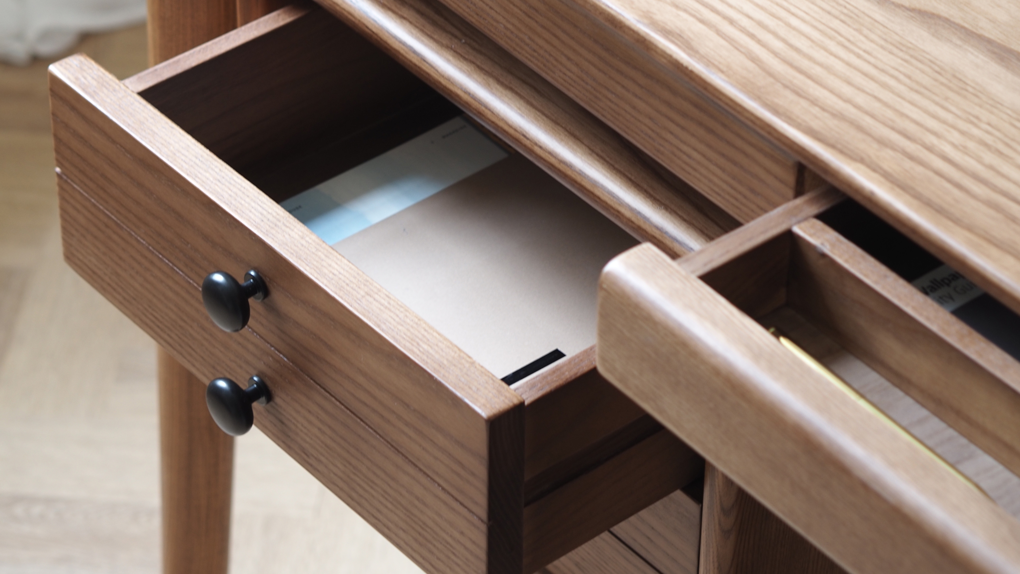 an open desk drawer on a wood desk with black handles