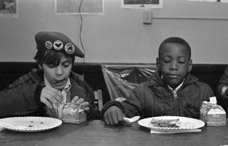 View of two young boys as they eat during a free breakfast for children program sponsored by the Black Panther Party, New York, New York, winter 1969.