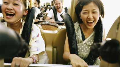 Two women happily scream with excitement on a roller coaster.