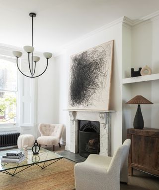 Contemporary, minimalist style living room, sculptural hanging pendant, white painted walls, large artwork placed above fireplace, dark wood herringbone flooring, textured rug, glass coffee table, two cream boucle lounge chairs