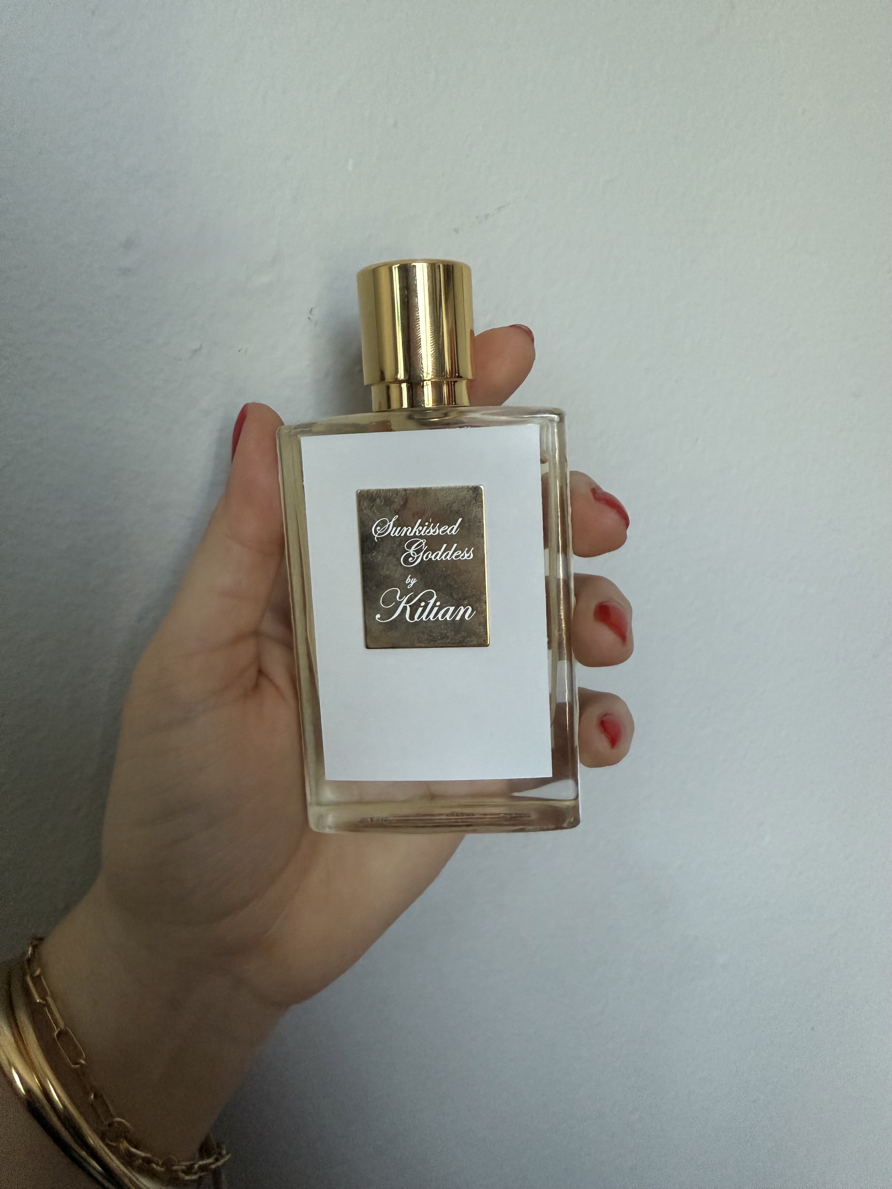hand holding up Kilian paris sunkissed goddess perfume bottle against grey wall