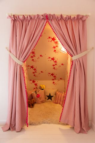 A little girls bedroom setup with floor to ceiling pink curtains tied back to reveal a cosy reading nook