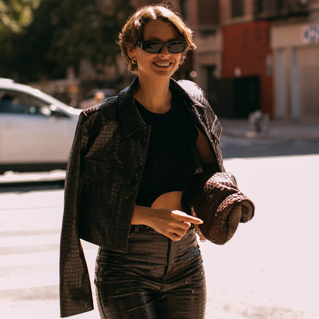 fashion week attendee wearing sunglasses and leather jacket over shoulders 