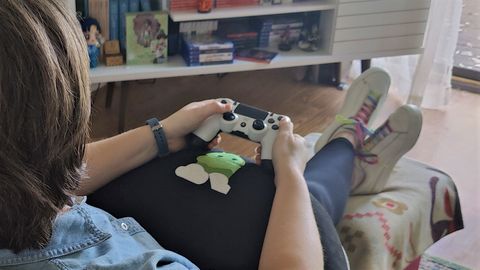 An over-the-shoulder view of a woman holding a PlayStation 4 controller in her hands while her wrists and elbows rest on the Valari Gaming Pillow