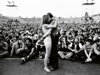 Black and white photo of David Bowie on stage in front of a large crowd hugging a woman fan.