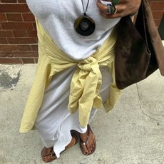 A woman wearing a white dress with brown flip flops and a brown pedicure