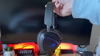 Reviewer hand holding the Asus ROG Delta II headset against a PC gaming setup