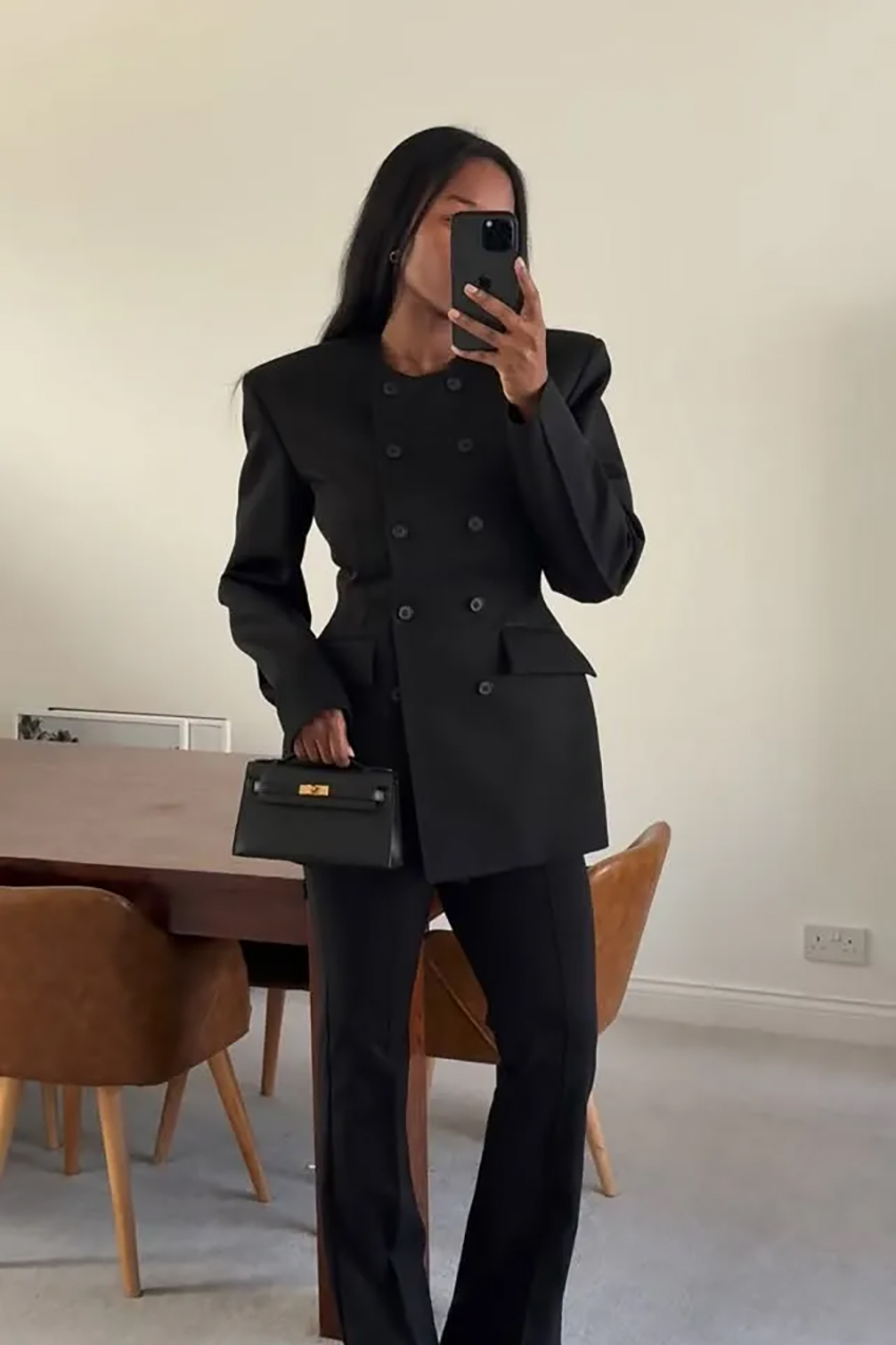 a woman wearing a black button-down waisted blazer and black pants