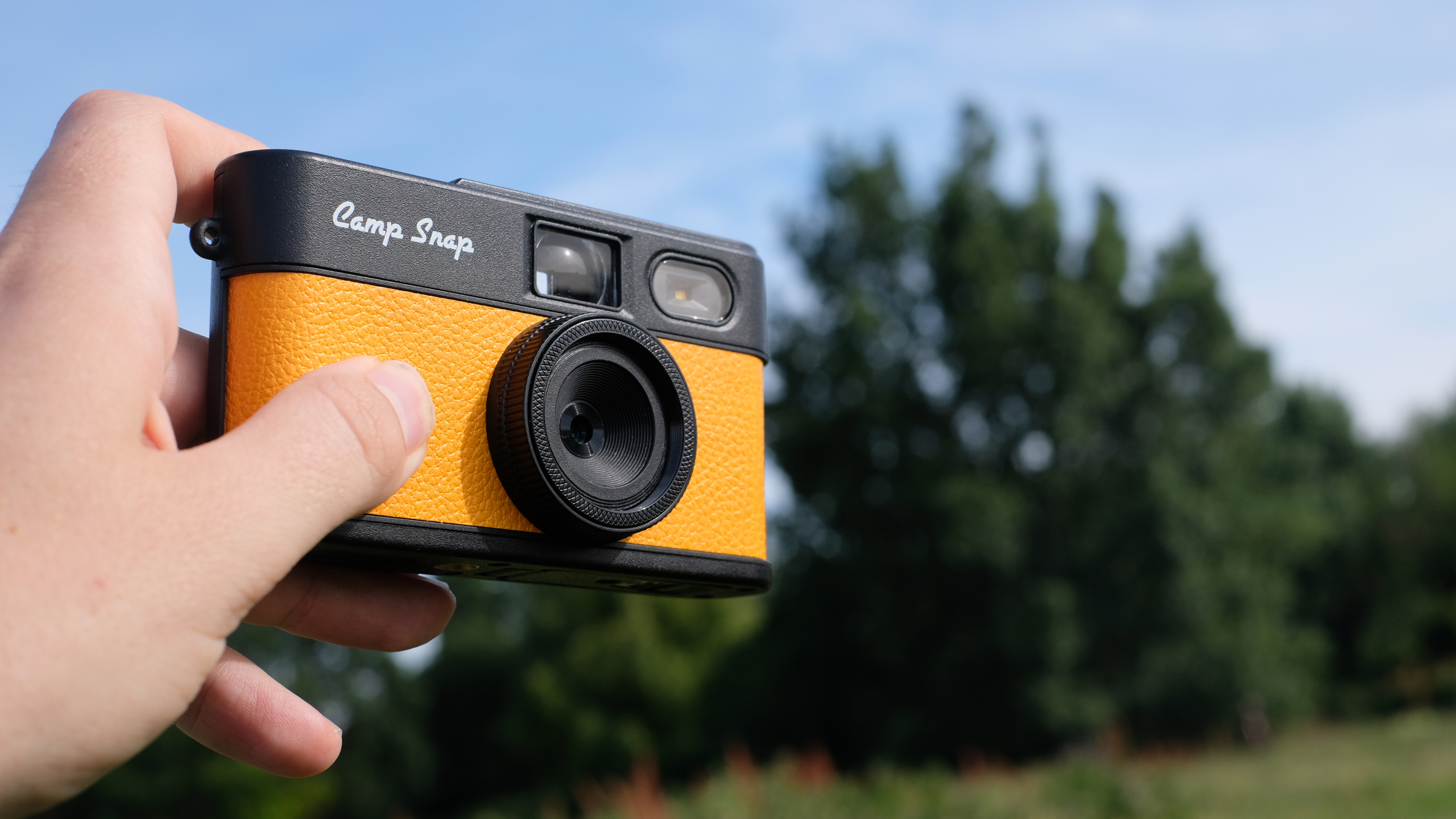 Photograph of man's hand holding Camp Snap 2 digital camera, in yellow colorway
