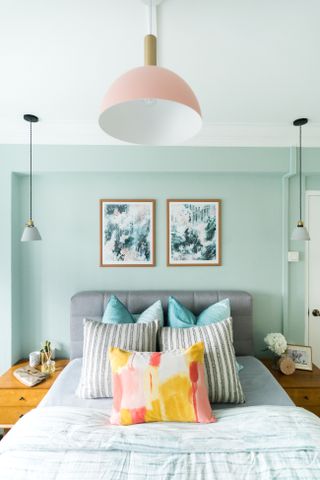 A bedroom with sage green walls, and a pink pendant light