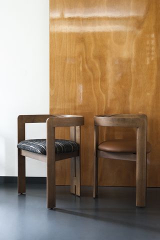 Shown on the floor against a wooden panel are two models of Tobia Scarpa's Pigreco chair, with upholstery options in striped textile or brown leather