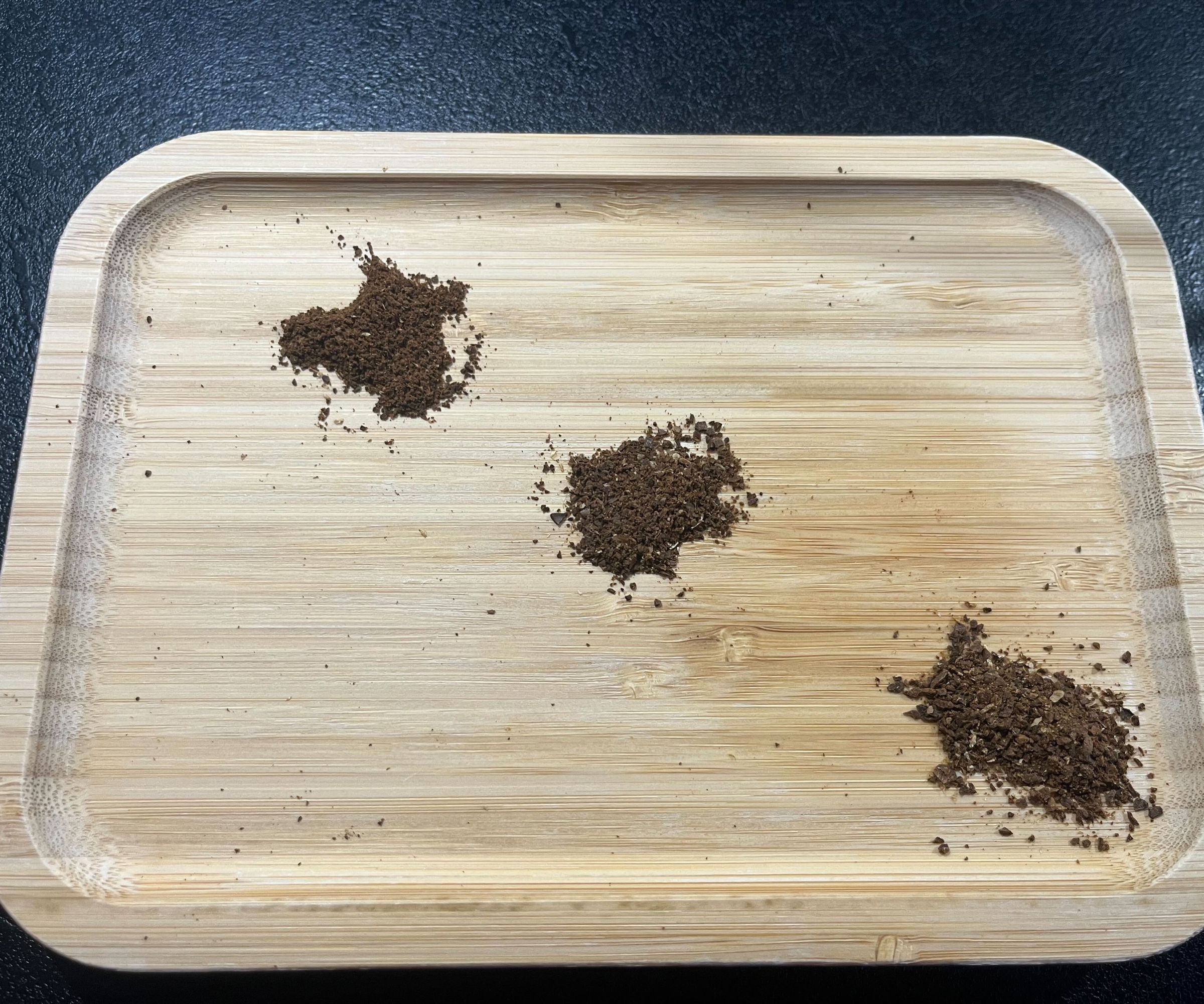 Three piles of coffee grinds ranging from find to medium on a wooden tray