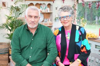 Paul Hollywood in a green shirt and Prue Leith in a multi-coloured top sit in the tent in The Great British Bake Off.