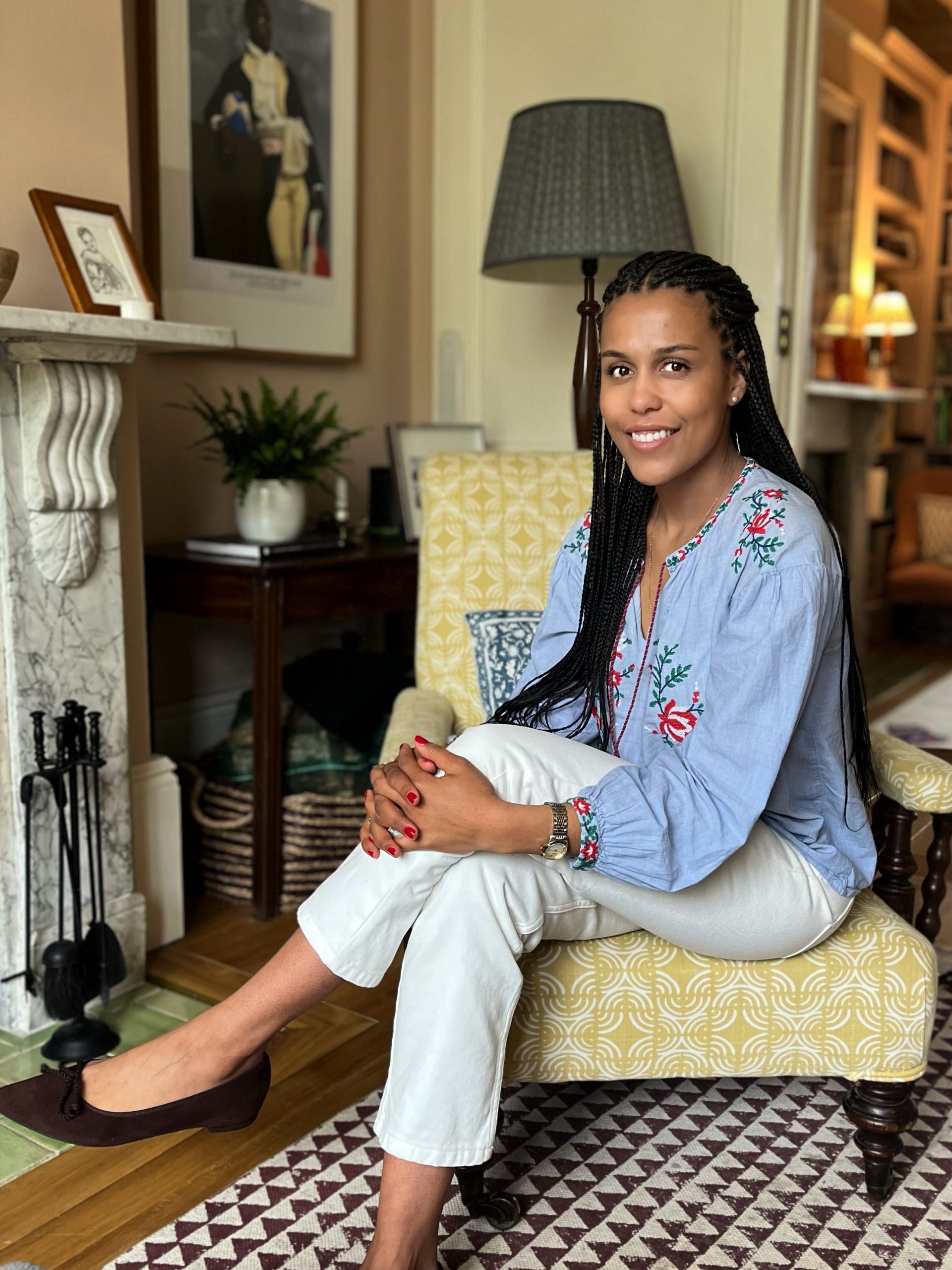 a woman sitting in a yellow armchair wearing a blue shirt and white pants