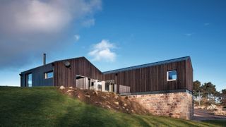 black timber clad and stone house on slope