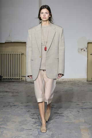 A model walking at Carven's spring/summer 2024 runway show wearing a natural-colored blazer, a sheer skirt, and tan square-toe mules.