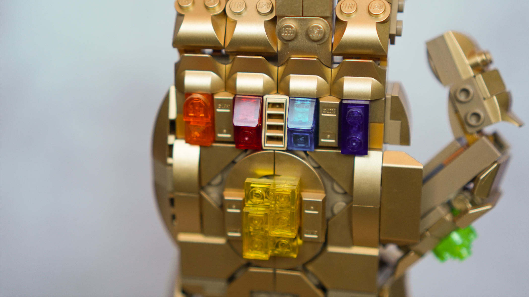 The back of a hand made of gold bricks features multi-colored stones and is placed in front of a grey background.