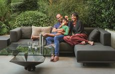a family sat on an outdoor sofa in front of a lush green backdrop