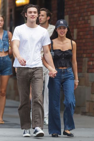 Olivia Rodrigo wears black ballet flats, a black tank, and jeans with a Yankees hat.