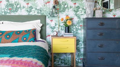 Small bedroom with yellow bedside table and colorful wallpaper