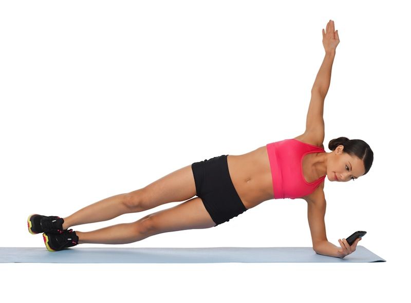 A woman exercises while holding her smartphone.