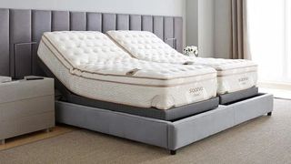 Image shows a Saatva Classic Split King Mattress on a beige fabric bedframe in a neutral colour bedroom