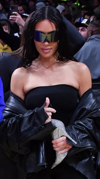 Kim Kardashian Lakers game in an all-black Balenciaga outfit carrying an embellished stiletto-style purse