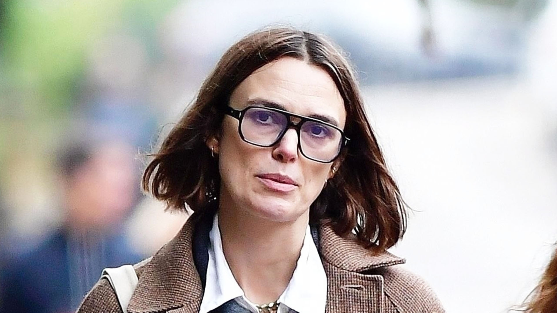 Kiera Knightly wearing a brown coat, navy polo, darkwash jeans, and black 