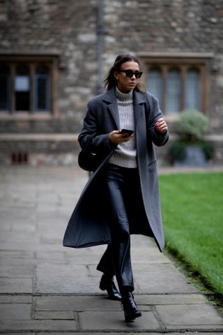 Woman wearing a gray turtleneck sweater, coat, leather pants, and boots