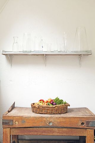 a wooden traditional butchers block with a basket full of veg on top of it, and a floating shelf above with glassware on it