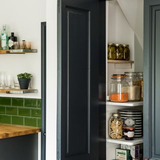 Narrow larder unit in a dark grey kitchen with green brick tiles