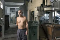 Man with one arm stood in abandoned factory. 