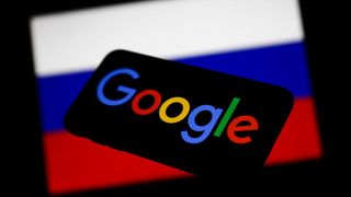 A smartphone with the Google logo displayed on screen floats in front of a blurred Russian flag