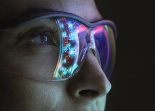 Female cyber security worker in a dark room with screen reflected on glasses. 
