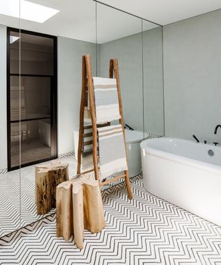 A bathroom with zigzag tile, freestanding bath and mirrored wall