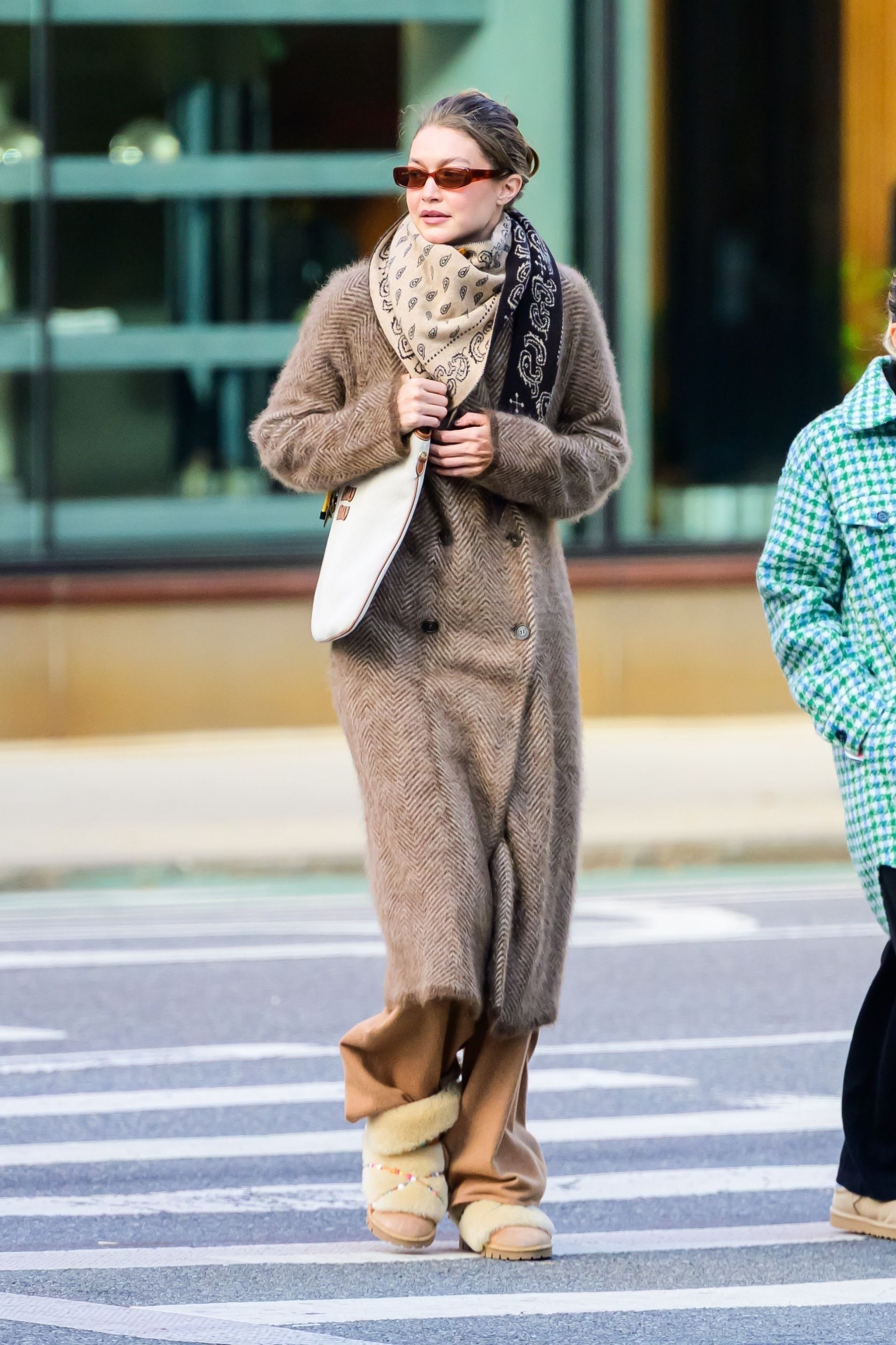Gigi hadid wears a silk scarf, wool coat, red sunglasses, miu miu bag, tan wide-leg pants, and inside out uggs boots.